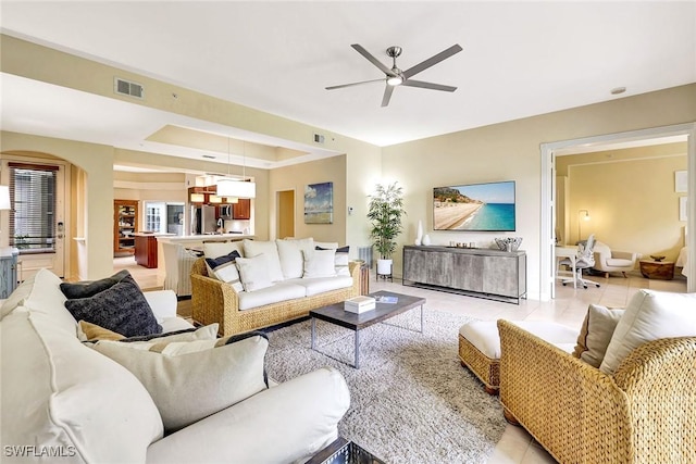 tiled living room featuring a raised ceiling and ceiling fan