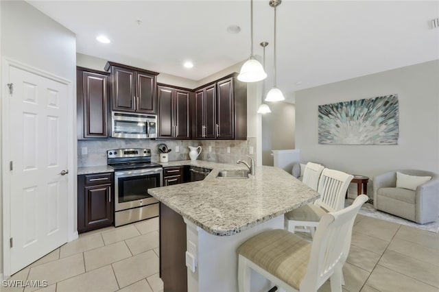 kitchen with a breakfast bar, a sink, backsplash, a peninsula, and appliances with stainless steel finishes