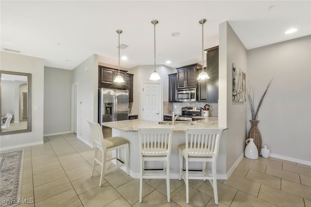 kitchen featuring appliances with stainless steel finishes, hanging light fixtures, light stone counters, tasteful backsplash, and dark brown cabinetry