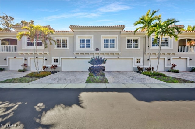 view of property featuring stucco siding, an attached garage, a tile roof, and decorative driveway