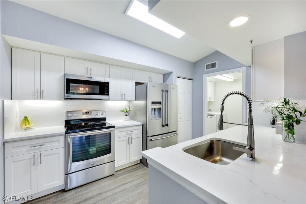 kitchen with lofted ceiling, sink, appliances with stainless steel finishes, white cabinetry, and tasteful backsplash