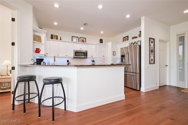 kitchen with dark wood-type flooring, dark stone countertops, appliances with stainless steel finishes, kitchen peninsula, and white cabinets