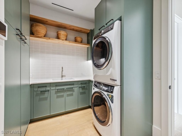 washroom with cabinets, stacked washer / dryer, sink, and light wood-type flooring