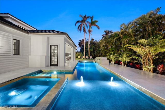 pool at dusk featuring a patio area and an in ground hot tub