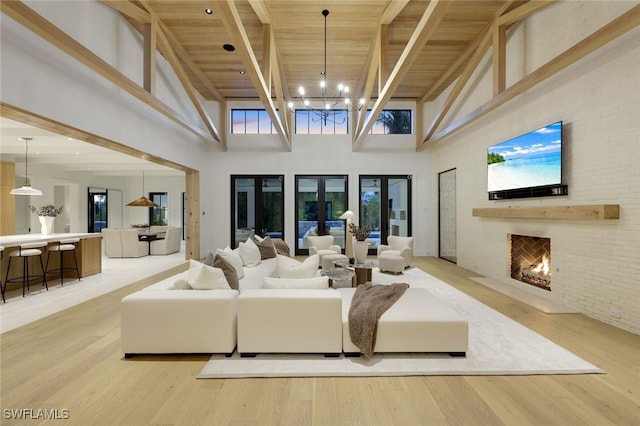 living room with an inviting chandelier, a brick fireplace, wooden ceiling, light hardwood / wood-style flooring, and a towering ceiling