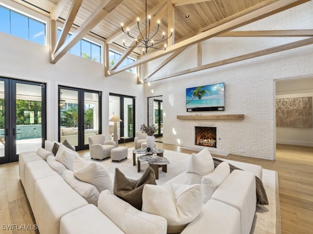 living room with a brick fireplace, beam ceiling, light hardwood / wood-style floors, and french doors