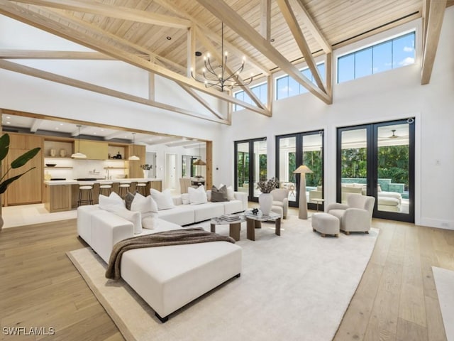 living room featuring beamed ceiling, an inviting chandelier, light wood-type flooring, and french doors