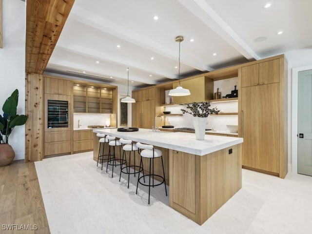 kitchen with a breakfast bar area, beamed ceiling, light hardwood / wood-style flooring, pendant lighting, and a large island