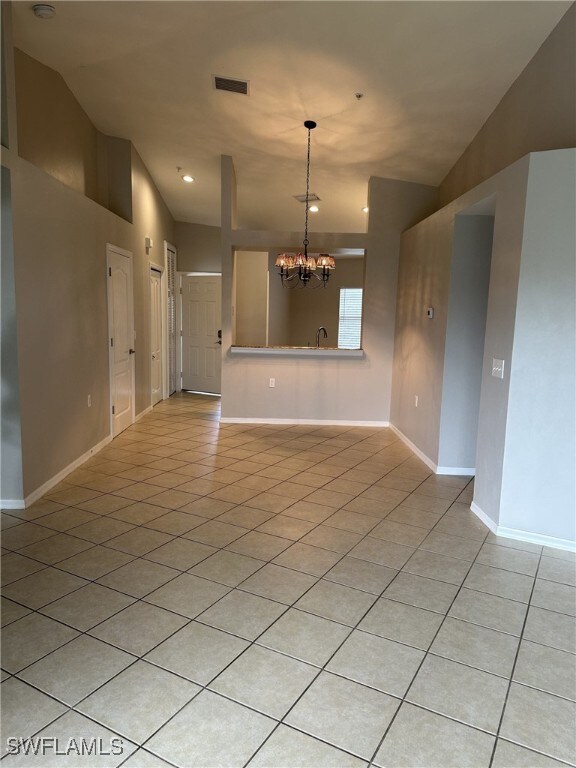 tiled spare room featuring lofted ceiling, sink, and a chandelier