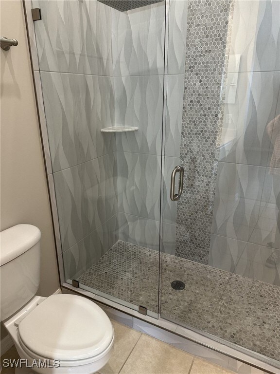 bathroom featuring toilet, an enclosed shower, and tile patterned flooring