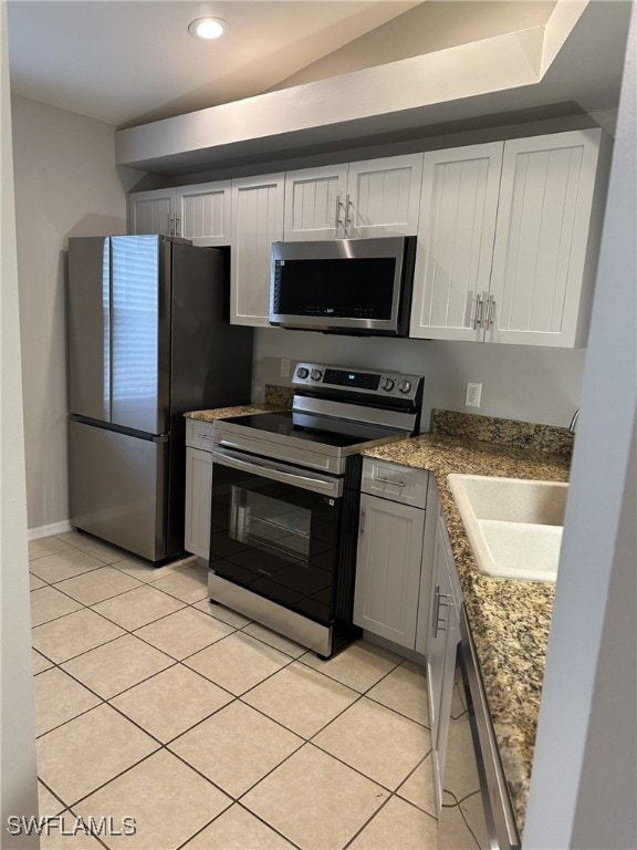 kitchen featuring sink, appliances with stainless steel finishes, white cabinetry, light tile patterned flooring, and dark stone counters