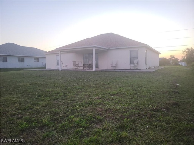 back of house featuring stucco siding, a lawn, and a patio area