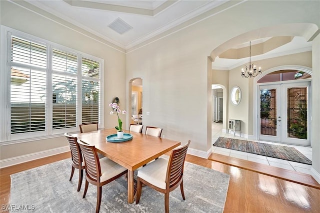 dining area with french doors, crown molding, a raised ceiling, a notable chandelier, and hardwood / wood-style floors