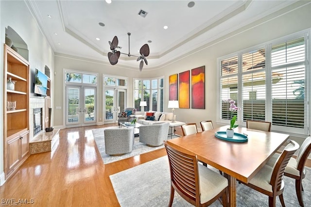 dining area featuring crown molding, light hardwood / wood-style floors, a raised ceiling, and french doors