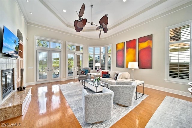 living room with ornamental molding, light hardwood / wood-style floors, a raised ceiling, a premium fireplace, and french doors