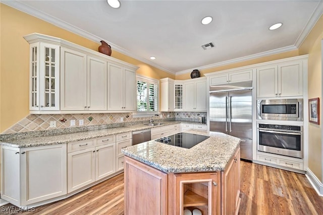 kitchen featuring light stone countertops, built in appliances, white cabinets, and backsplash