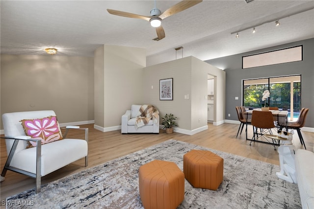 living area featuring a textured ceiling, light wood-type flooring, lofted ceiling, and baseboards