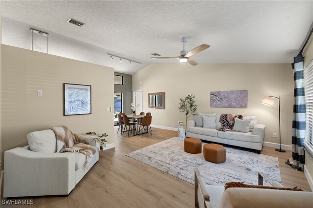 living room with vaulted ceiling, rail lighting, ceiling fan, a textured ceiling, and light hardwood / wood-style flooring