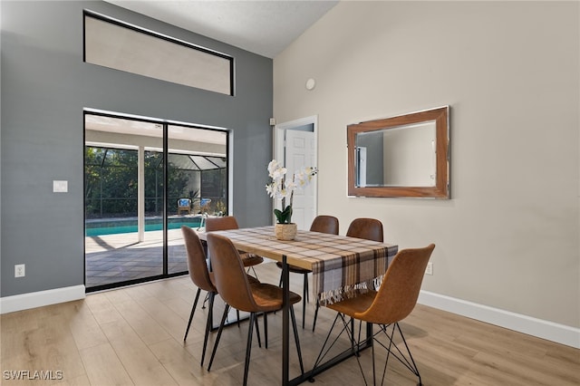 dining room featuring a towering ceiling, light wood finished floors, and baseboards