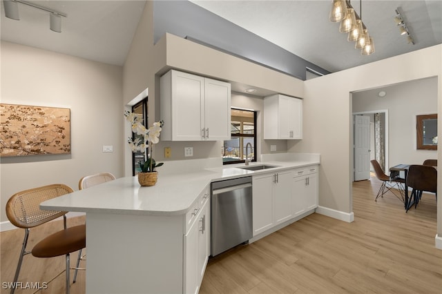 kitchen featuring a breakfast bar, a peninsula, light countertops, white cabinetry, and stainless steel dishwasher