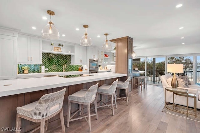 kitchen with white cabinetry, a kitchen breakfast bar, hanging light fixtures, black electric stovetop, and light hardwood / wood-style flooring