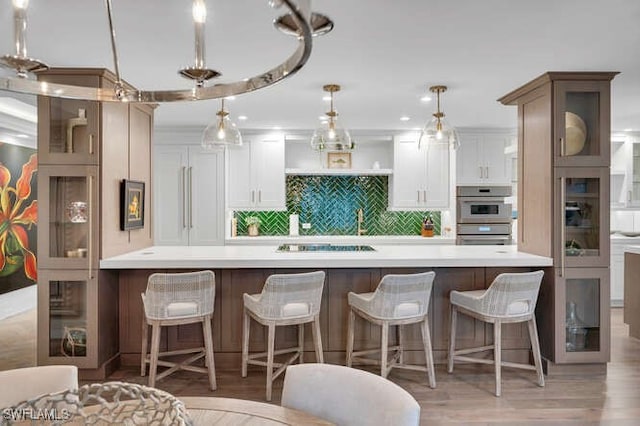 kitchen featuring double oven, white cabinetry, decorative backsplash, hanging light fixtures, and light wood-type flooring