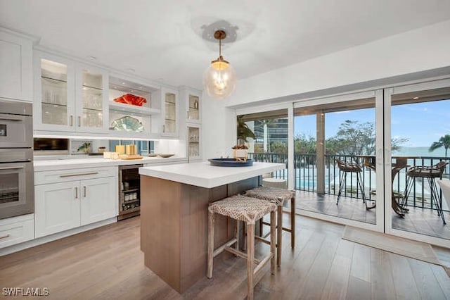 kitchen featuring wine cooler, a water view, decorative light fixtures, light hardwood / wood-style flooring, and white cabinets