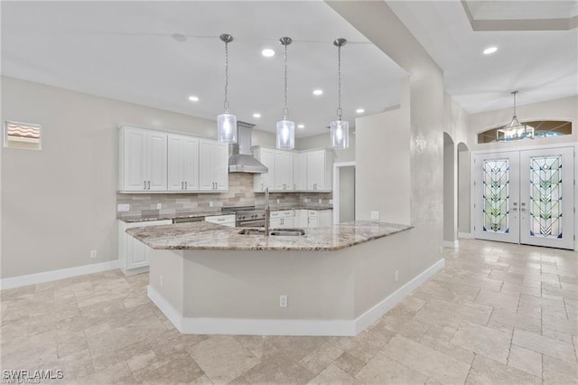 kitchen featuring white cabinetry, wall chimney range hood, and light stone counters