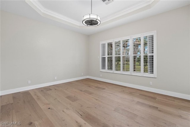 empty room featuring crown molding, light hardwood / wood-style floors, and a raised ceiling