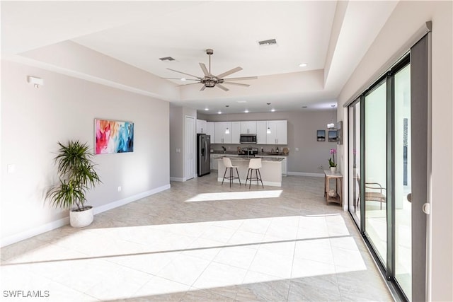 kitchen featuring a breakfast bar area, a center island, appliances with stainless steel finishes, a tray ceiling, and white cabinets