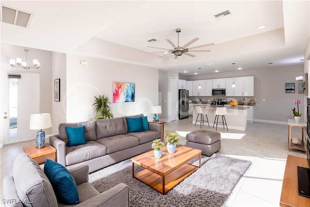 tiled living room with ceiling fan with notable chandelier and a raised ceiling