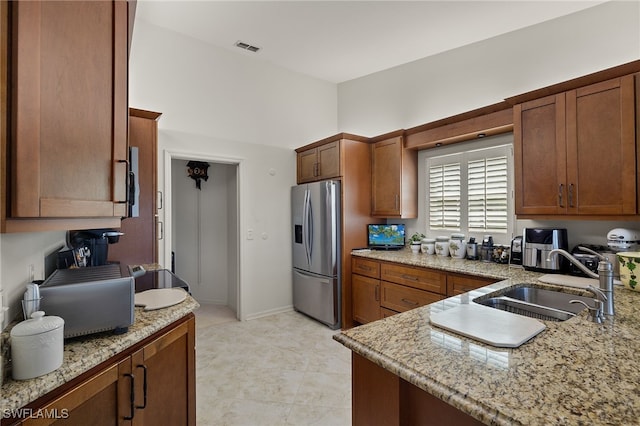 kitchen with light stone counters, stainless steel fridge with ice dispenser, and sink