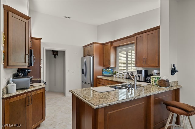 kitchen with sink, light stone counters, appliances with stainless steel finishes, a kitchen breakfast bar, and kitchen peninsula