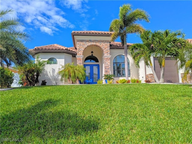 mediterranean / spanish home with a garage, stone siding, a front lawn, and french doors