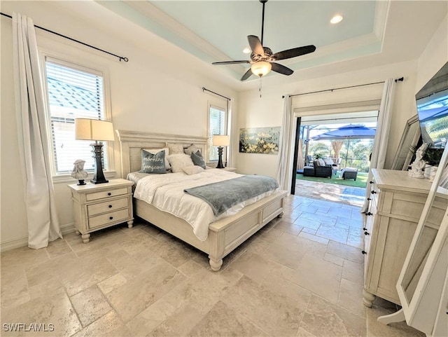 bedroom featuring stone tile floors, a ceiling fan, baseboards, access to outside, and a tray ceiling