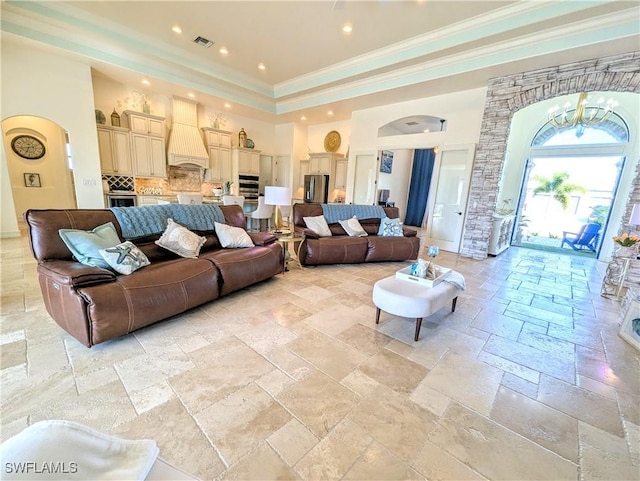 living area with a notable chandelier, stone tile floors, visible vents, a towering ceiling, and ornamental molding