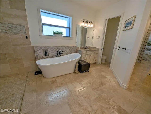 bathroom with tile walls, toilet, stone finish flooring, vanity, and a freestanding tub