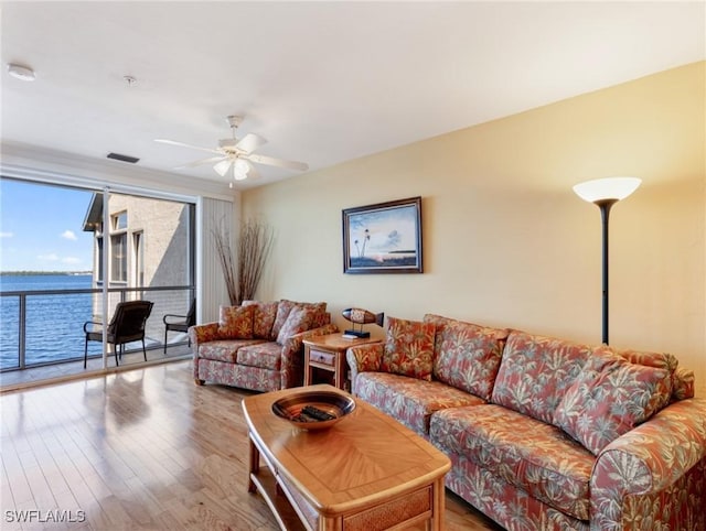 living room featuring wood-type flooring, a water view, ceiling fan, and a wall of windows