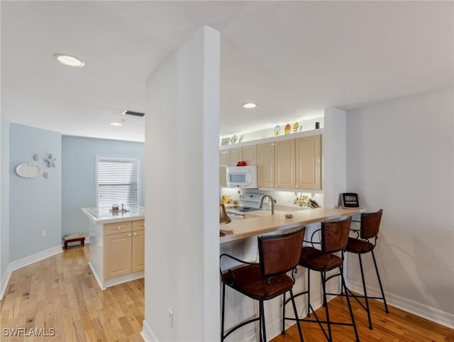 kitchen with white appliances, a breakfast bar, kitchen peninsula, and light hardwood / wood-style flooring