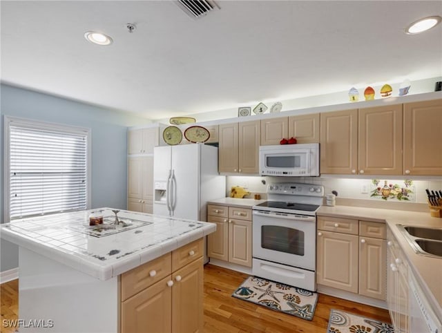 kitchen featuring sink, white appliances, light hardwood / wood-style flooring, a center island, and tile countertops