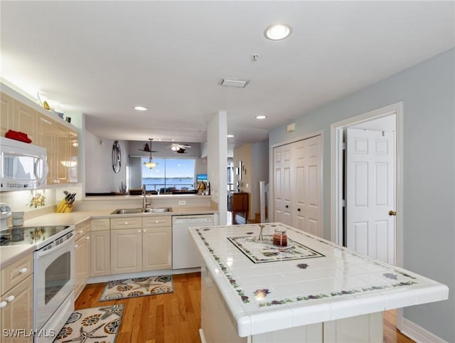 kitchen with sink, light hardwood / wood-style flooring, tile counters, a kitchen island, and white appliances