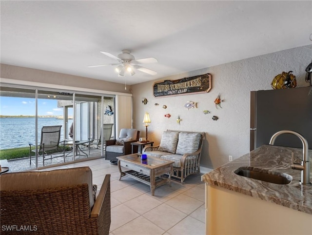 living room featuring a water view, sink, light tile patterned floors, and ceiling fan