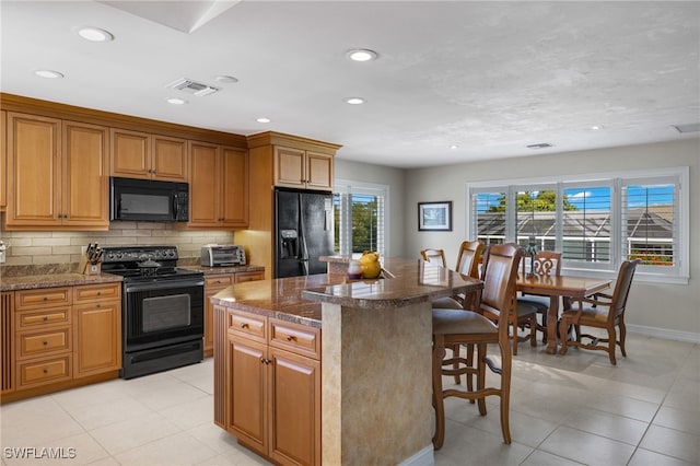 kitchen with a breakfast bar area, dark stone countertops, a center island, tasteful backsplash, and black appliances