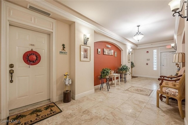 foyer with arched walkways, ornamental molding, visible vents, and baseboards