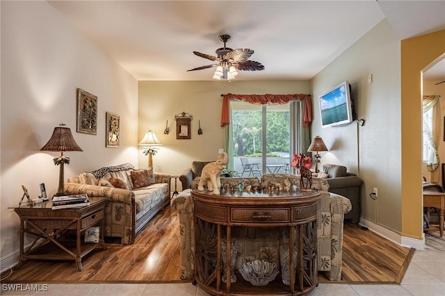 living area featuring arched walkways, ceiling fan, light wood-type flooring, and baseboards