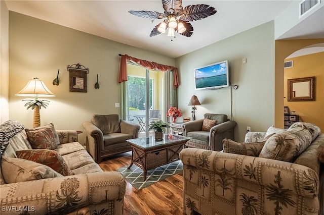 living room with ceiling fan, arched walkways, dark wood finished floors, and visible vents