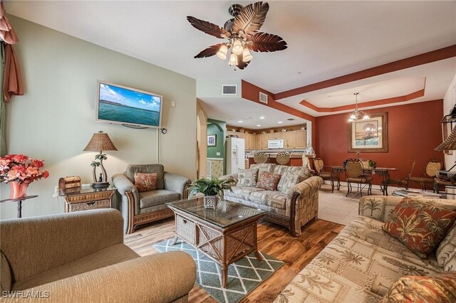 living area with light wood finished floors, visible vents, a tray ceiling, and ceiling fan with notable chandelier