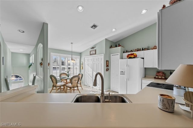 kitchen featuring pendant lighting, white cabinets, lofted ceiling, and white fridge with ice dispenser