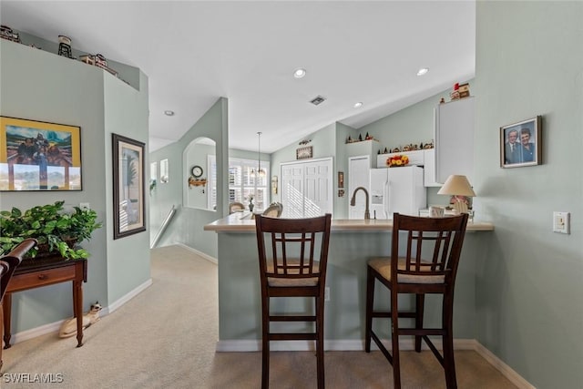 kitchen with a breakfast bar, pendant lighting, white cabinets, white fridge with ice dispenser, and kitchen peninsula