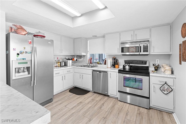 kitchen featuring sink, light wood-type flooring, a tray ceiling, stainless steel appliances, and white cabinets